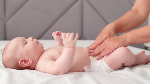 Mother changing diaper on her newborn baby. Mother changing diaper on her newborn baby indoors. The child moves his legs.  Dry skin.  Mom puts diapers on her newborn baby on a changing table.