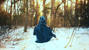 Fantasy woman runs in winter forest. Princess girl. Blue long vintage dress fabric waving, hood on head. back rear view silhouette wanderer stroll along path. Nature pine tree snow sun divine light