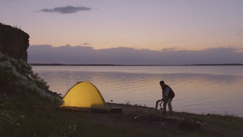 Horizontal long shot of young Caucasian man and woman preparing for overnight stay in camping on lakeshore