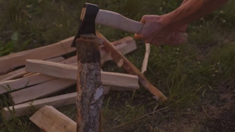 Horizontal shot of unrecognizable tourist chopping firewood for campfire in evening