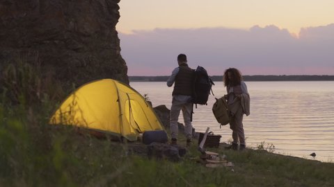 Horizontal shot of young Caucasian man and woman preparing for overnight stay in camping on lakeshore