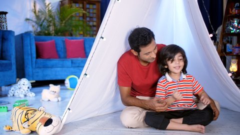 A young man and his little son in casual clothes doing a fun activity under a canopy - Single father, Indian father . A spacious living room with colorful soft toys lying on the floor - leisure tim...