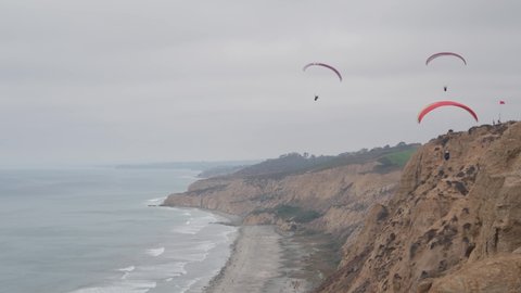 People paragliding, Torrey Pines cliff or bluff. Paraglider soaring in sky air on parachute, kite or wing. Sport hobby. Ocean coast, San Diego, California USA. Para gliding risky flight. Birds flying.