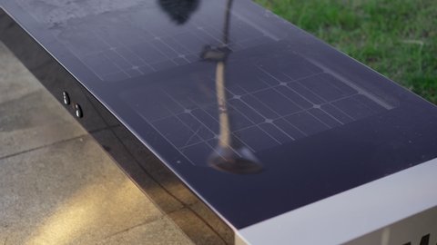 A smart bench with a smartphone laying on it. A smart bench has solar panels on its top and can charge USB devices for free