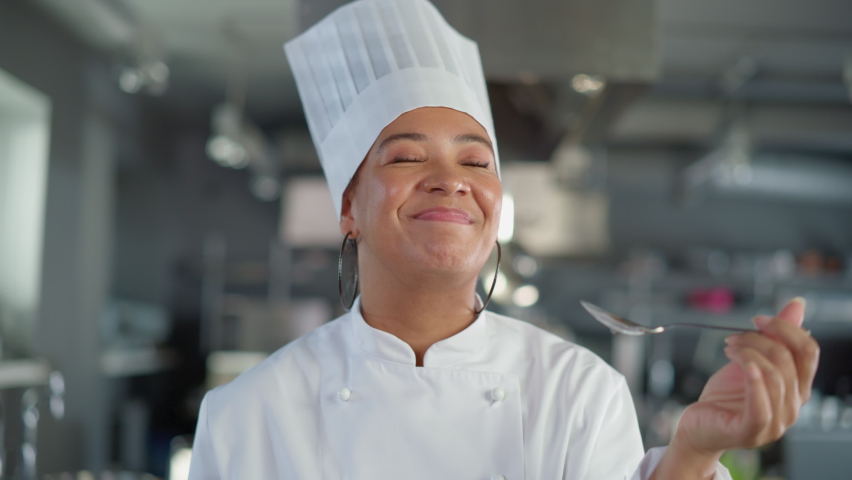Restaurant Kitchen: Portrait of Black Female Chef Preparing Dish, Tasting Food and Enjoying it. Professional Cooking Delicious, Authentic, traditional Food, using Healthy Ingredients for Meal Recipe