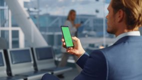 Airport Terminal: Businessman Working on Green Chroma Key Screen Mobile Smartphone, Waits for a Plane Flight. Entrepreneur Does Online Remote Work in Boarding Lounge of Airline Hub. Over the Shoulder - Powered by Shutterstock - Get 15% off with code: PIKWIZARD15