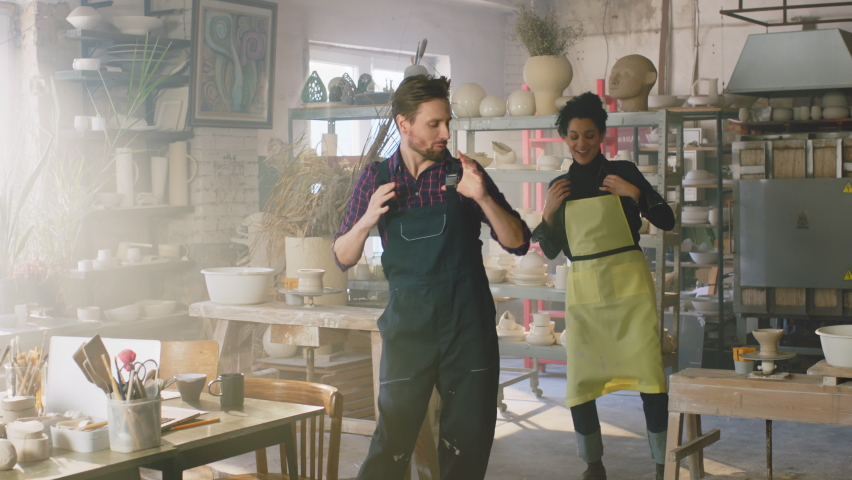 Two young colleagues, woman and man, have fun at work, dancing together in pottery studio, enjoying a short break and sharing positive vibes, Slow motion.