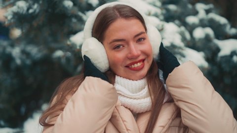 Close up portrait young woman with fur earmuffs winter day outdoor. Beautiful caucasian female looking camera and smile