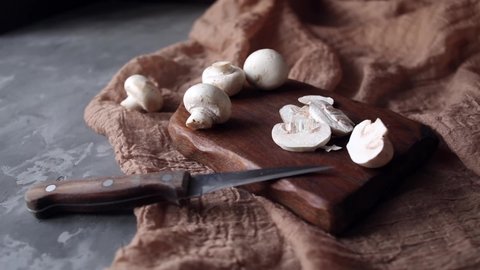 Fresh white champignons on a cutting board on a brown textile background. Knife next to champignons cut into slices. Kitchen, cooking, recipes. Mushrooms, ingredient. Gray background