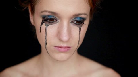 Young woman crying on black background. Woman with black mascara running under her eyes