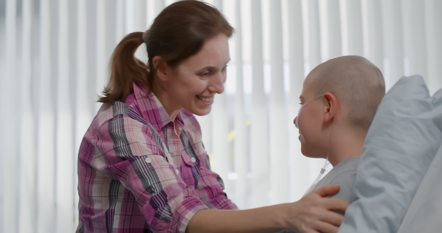 Mother visiting teen son with cancer in hospital ward. Side view of bald kid resting in hospital bed and hugging mother visitor. Healthcare and medicine concept Royalty-Free Stock Footage #1086654032