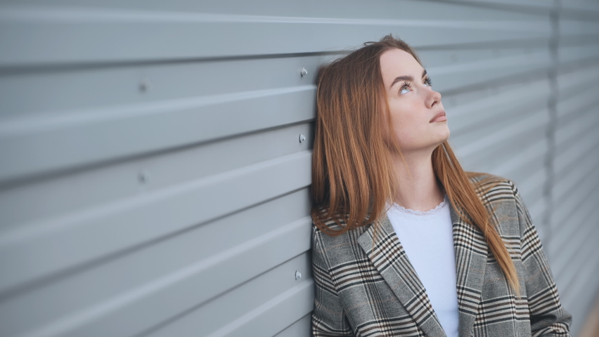 A pensive, sad girl at the striped wall of the house.