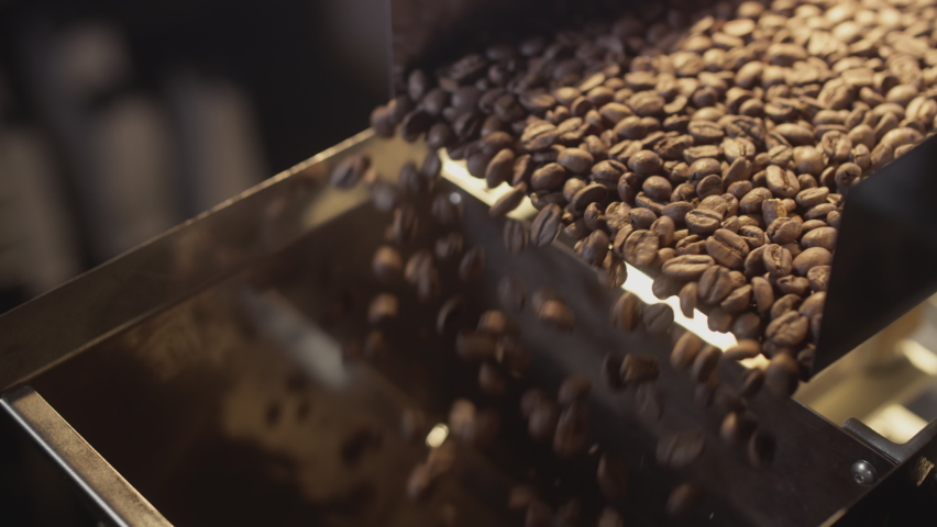 Roasted coffee beans fall out of the chiller. Arabica beans are poured and rotated. Industrial roasting and production, coffee industry. Close-up, brown grains fall down to be filled into packages. Royalty-Free Stock Footage #1086655049