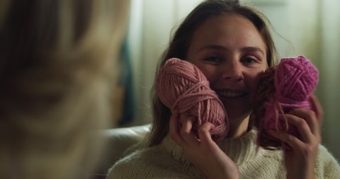Cinematic close up of adult daughter tries softness of balls of wool while knitting together with her mature mother warm yarn wool with knitting needles while sitting comfortably on sofa at home.