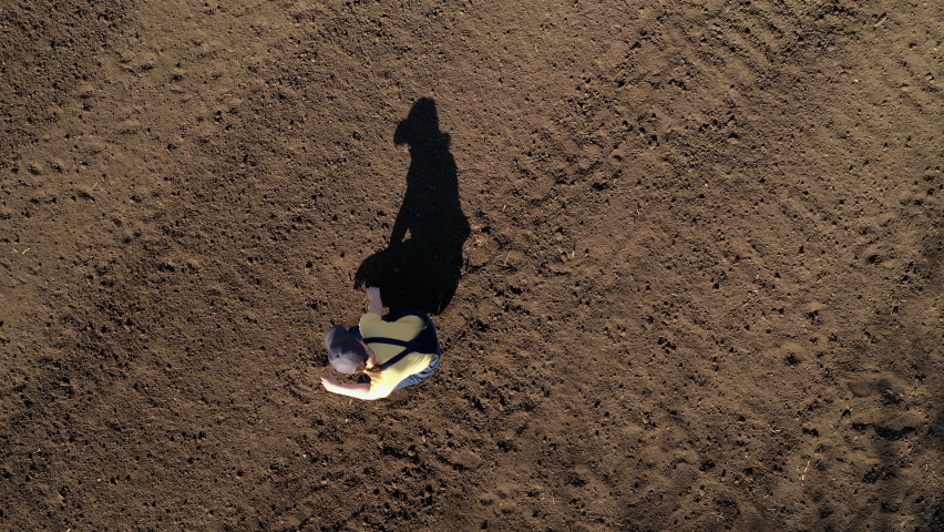 Female farmer examining ploughed field soil, drone footage top view of woman agronomist working casting shadow on theground | Shutterstock HD Video #1086657281