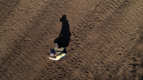 Female farmer examining ploughed field soil, drone footage top view of woman agronomist working casting shadow on theground