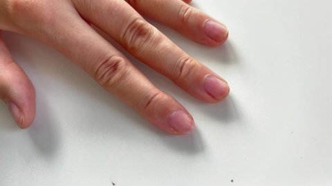 Making manicure at home. Close-up footage of hand using cuticle pusher to push cuticle on nails on white background.