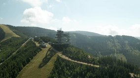 180 degrees orbit aerial shot of a sky walk tower attraction in Dolni Morava, Czech Republic and a nearby MTB bicycle trail. The drone is moving slowly to the right.