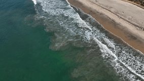 Tilt up video of waves crashing on sandy beach along the coastline and the beautiful town of Carlsbad, California, USA.