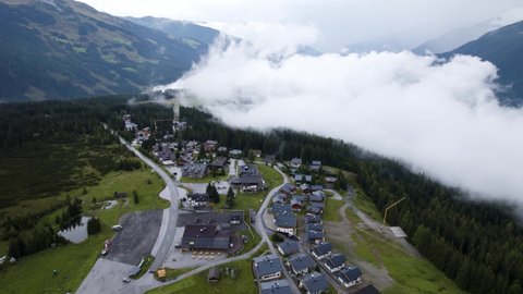 Aerial drone view of small Austrian ski village high in valley between mountains and mist in Krimml