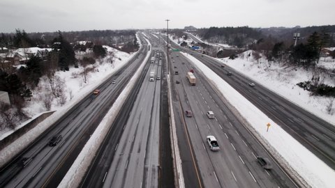 Tracking Aerial Flyover of Busy Winter Highway with blowing Snow and transport trucks in Scarborough Toronto East 401, Overcast Day
