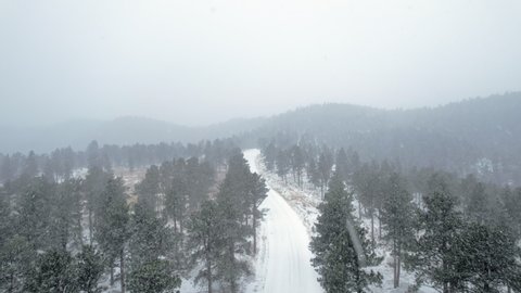 Drone Aerial Footage Over Snowcapped Country Road Surrounded by Pine Trees near Flatirons Mountain in Boulder Colorado USA During Foggy Snowstorm Blizzard.