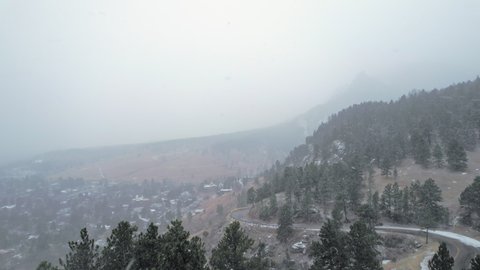 Drone Aerial Footage Over Snowcapped Pine Tree Hillside Road near Flatirons Mountain in Boulder Colorado USA During Foggy Snowstorm Blizzard.
