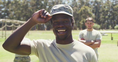 Portrait of smiling african american male soldier in cap at obstacle course with others behind him. healthy active lifestyle, cross training outdoors at boot camp.