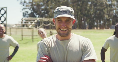 Portrait of caucasian male soldier in cap smiling at obstacle course with diverse group behind him. healthy active lifestyle, cross training outdoors at boot camp.
