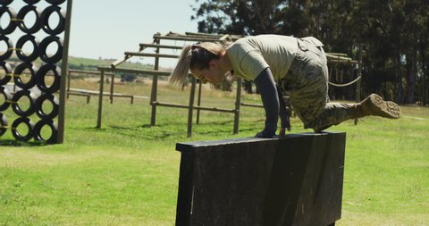 Fit caucasian female soldier exercising on obstacle course, climbing over fence and running. healthy active lifestyle, cross training outdoors at boot camp.