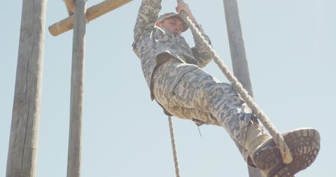 Caucasian male soldier in uniform climbing down rope on military obstacle course in sun. healthy active lifestyle, cross training outdoors at boot camp.