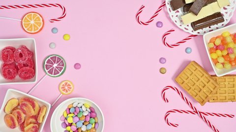 6k Candies chocolates, gummy candies and lollypops appear on left and right side of pastel pink background. Stop motion animation flat lay