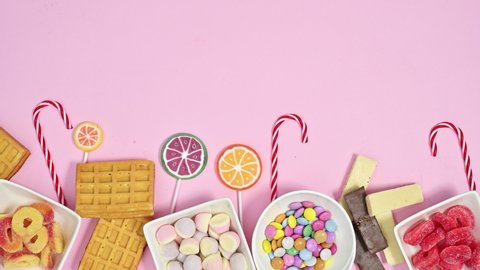 6k Sweet colorful desserts, gummy and chocolate candies and lollypops move on bottom of pastel pink background. Stop motion animation flat lay