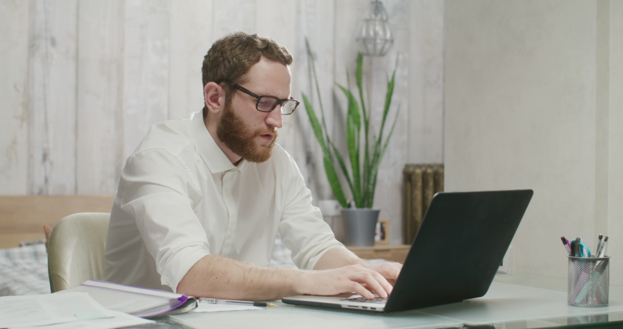 serious tired man working on a laptop. Young male professional using computer sitting at home office desk. Busy worker freelancer working on modern tech notebook device. Royalty-Free Stock Footage #1086670091