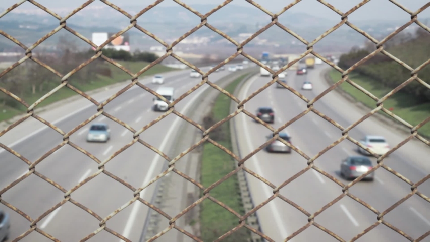 Vehicles are moving on the highway behind pattern of wire mesh fence. Traffic and transportation concept. | Shutterstock HD Video #1086671066
