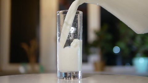 Pouring natural milk from a jug into a glass on a turntable, fresh dairy product in a glass, pouring milk in slow motion.