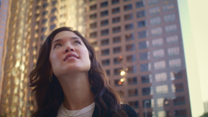 Portrait of smiling woman looking up on great modern buildings megapolis. Attractive asian female exploring city on summer weekend close up. Gorgeous model posing in stylish clothes standing on street | Shutterstock HD Video #1086672995