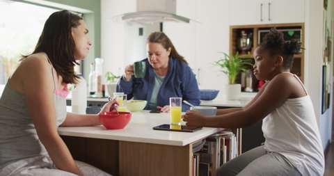 Happy caucasian lesbian couple and their african american daughter eating breakfast in kitchen. domestic life, spending time at home.