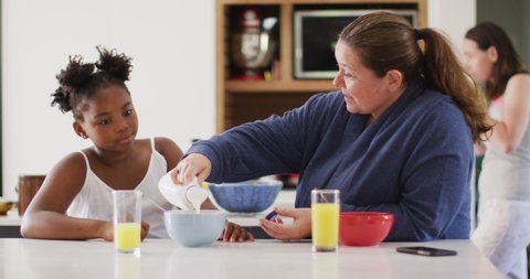 Happy caucasian lesbian couple and their african american daughter eating breakfast in kitchen. domestic life, spending time at home.