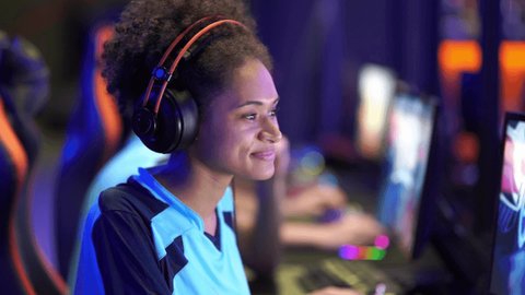 Happy female gamer showing thumb up sign and smiling while using powerful computer for online game in computer club