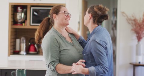 Caucasian lesbian couple smiling and dancing in kitchen. domestic life, spending free time relaxing at home.