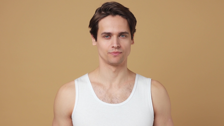 Smiling young man 20s perfect skin wears white tank top hold point on apple show thumb up isolated on plain pastel beige background studio portrait. Skin care healthcare cosmetic procedures concept Royalty-Free Stock Footage #1086675965