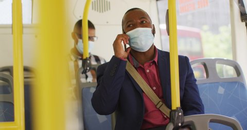 African american man in city wearing face, using smartphone and smartwatch in bus. digital nomad on the go, out and about in the city during covid 19 pandemic.