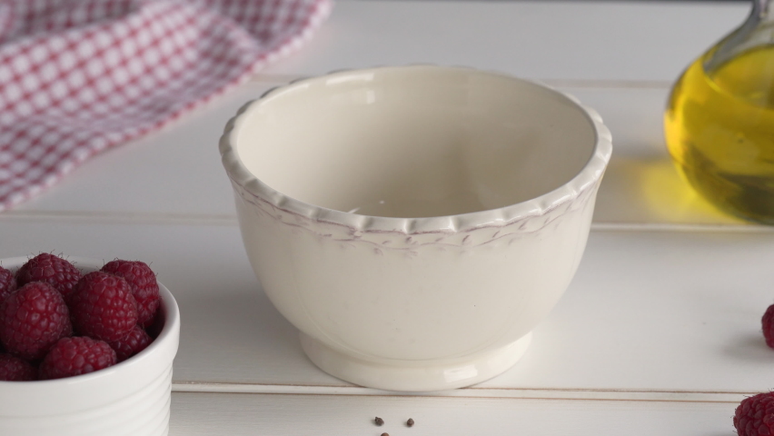 Pouring cottage cheese blended with flax seed oil into a bowl, with fresh raspberries in the foreground