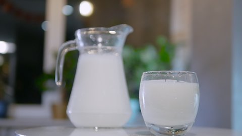 Slow motion glass with fresh milk on bokeh background. A natural dairy product in a jug and in a glass is spinning on the table
