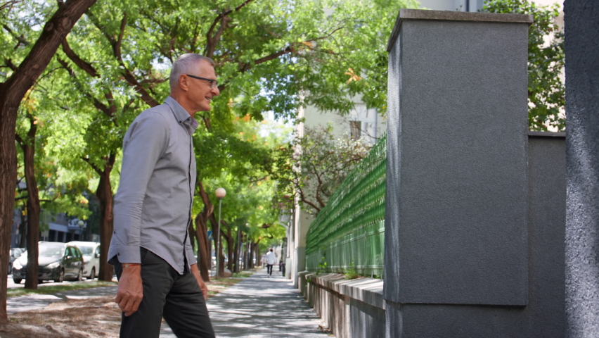 Happy schoolboy running to his grandfather waiting for him after school outdoors in street.