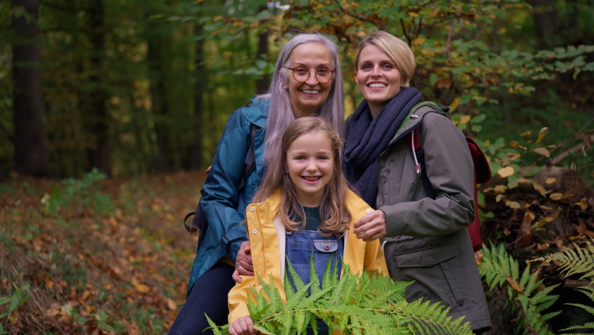 Small girl with mother and grandmother on walk outoors in forest, looking at camera.