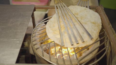 Asian trader is roasting Kite crackers (Kaw Kriab Wow) on street food night market. charcoal grill Kite cracker snack Thai dessert stove.