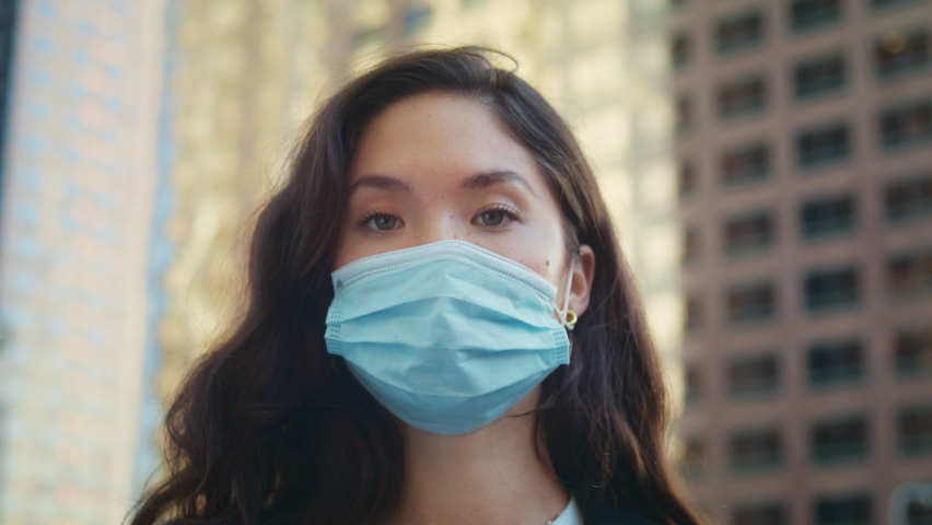 Attractive brunette woman taking off face medical mask on town street closeup. Young asian lady smiling looking on camera without protection equipment. Concept safety healthy life in pandemic.