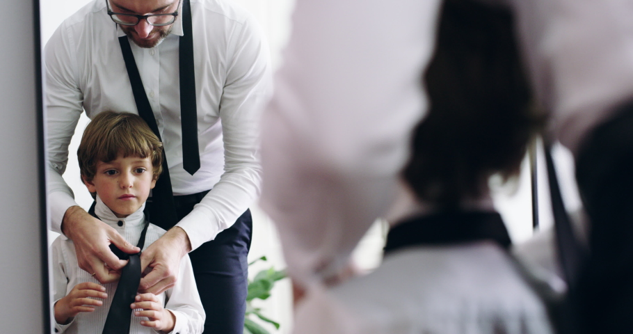 Who better to learn about style than from dad. 4k video footage of an adorable little boy and his father getting dressed in matching suits at home.